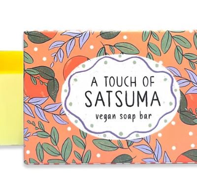 Floral and Leaf Pattern Soap Bar Packaging on Vibrant Orange Background - Featuring A Touch of Satsuma Vegan Soap Bar Label. Discover the partially open package revealing a pale yellow Gingerbread Soap Bar for a luxurious bathing experience. Perfect for eco-conscious buyers seeking beautiful soap packaging and vegan-friendly ingredients.