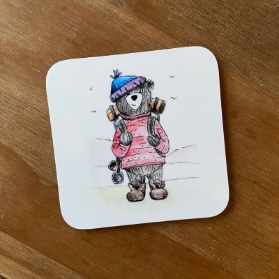 Introducing the Hiker Bear Coaster: this charming drink coaster showcases a bear hiker sporting a pink sweater and blue beanie, complete with headphones wrapped around its neck and holding a music player for the ultimate outdoor adventure. The delightful design is set against a natural wooden background, making it the perfect addition to any nature lovers home decor.