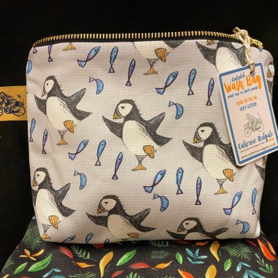 The Dancing Puffin Wash Bag showcases an enchanting puffin and fish design, perfect for nature enthusiasts. This stylish wash bag features a beige label with a blue border, proudly displaying Wash Bag and Celtic House. Enhanced by a lively leafy motif backdrop, this puffin-themed accessory is both functional and fashionable for travel or daily use.