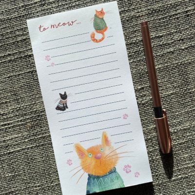 The To Meow Cats List Pad offers a delightful writing experience with its to meow... header adorning lined pages. This unique notepad features adorable cats in sweaters and charming paw prints, making it a purr-fect choice for cat lovers. The set is complete with a stylish copper-finished pen, beautifully presented on a textured gray background, ideal for home or office use.