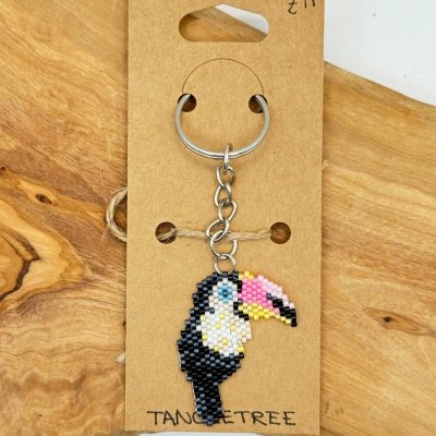 Discover our vibrant toucan beaded keychain, a stunning handmade accessory perfect for adding flair to your keys. This colorful toucan keychain is meticulously crafted with small beads and comes attached to a durable silver keyring. Presented on a stylish brown card featuring the TANCETREE brand, this unique piece is available for just £11. Enhance your collection with this artistic keyring today!.