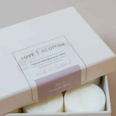 A beautifully designed white box displays a label with the keywords Love | Scottish Natural Blended Wax Melts, Hand-Poured with Love, Made in Scotland. Inside the box, youll find two round white wax melts elegantly labeled No.5 Scottish Rose, highlighting their authentic Scottish craftsmanship and natural ingredients.
