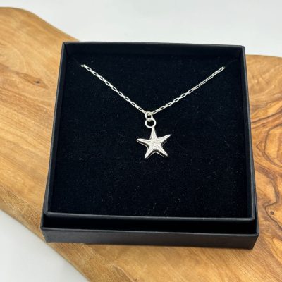 A stunning sterling silver star shaped necklace is elegantly displayed in a black jewelry box against a wooden background, enhancing the sophisticated design of this elegant silver accessory.