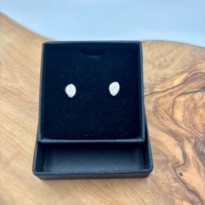 A set of petite textured sterling silver stud earrings is elegantly displayed in an open black jewelry box on a polished light wood surface.