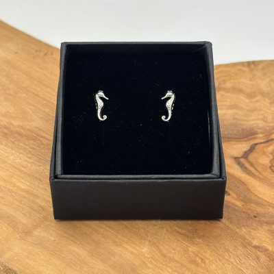 A stunning, sterling silver seahorse stud earring set is showcased in a black gift box, elegantly displayed on a rustic wooden surface.