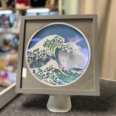 Explore our stunning framed artwork featuring a stylized wave inspired by traditional Japanese art. This exquisite piece showcases layered paper that creates a captivating three-dimensional effect. Perfectly displayed on a stand, this unique art piece stands out against its subtly blurred background, making it an ideal addition to any artistic or home decor setting.