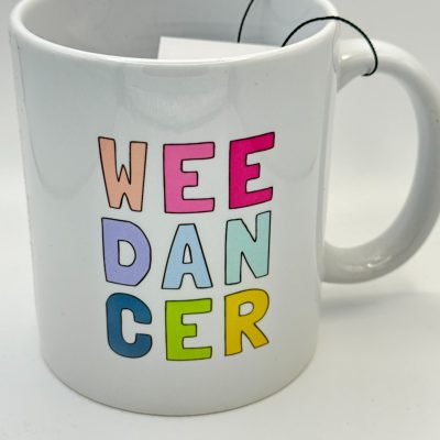 A white coffee mug featuring vibrant, pastel letters spelling WEE DANCER vertically. A tea bag string casually drapes over the side.