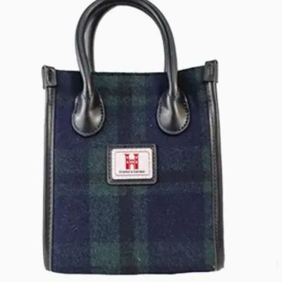 Check out our stylish small handbag with a dark green and navy checkered pattern, perfect for fashion enthusiasts. This trendy handbag features luxurious black leather handles and trim, making it an ideal choice for a chic yet classic look. The front of the bag is adorned with a distinctive red logo patch proudly displaying Harris Tweed, adding an authentic touch to this elegant accessory. Perfect for those searching for fashionable handbags or Harris Tweed bags online!.