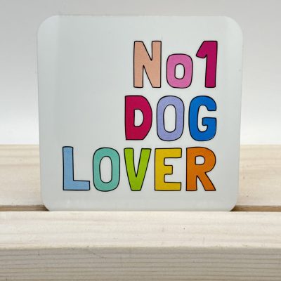 A vibrant No 1 Dog Lover coaster, featuring bold, colorful letters, rests on a light wood surface. The backdrop is a simple, neutral tone for an enhanced visual appeal.