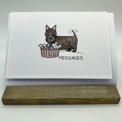 A beautifully illustrated greeting card on a rustic wooden stand showcases a black dog beside a bone-filled basket. The prominent MESSAGES text adds a charming touch to this unique dog-themed greeting card, perfect for pet lovers and gift enthusiasts.