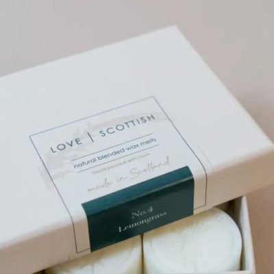 Discover the Love Scottish wax melts, beautifully displayed in a close-up view. This eco-friendly box of natural blended wax melts proudly highlights its origins with labels reading Made in Scotland. Featured in this collection is the refreshing scent of No.4 Lemongrass. The image reveals glimpses of the pristine white wax melts, promising aromatherapy and a touch of Scottish craftsmanship.