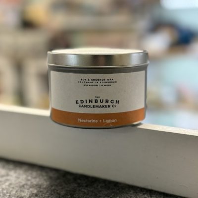 Introducing the Edinburgh Candlemaker Co. Tin Candle featuring the refreshing scent of Nectarine + Lemon. This premium candle, crafted from natural soy and coconut wax, is hand poured in Scotland to ensure quality and sustainability. Set on a stylish gray surface with a soft-focus background, this eco-friendly candle will enhance your ambiance while providing a delightful fragrance. Perfect for those seeking unique candles with sustainable ingredients that are hand made in Scotland.