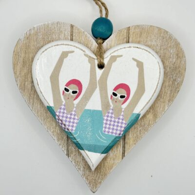 Discover a charming heart-shaped wooden decoration featuring an eye-catching illustration of synchronized swimmers. These athletes, wearing vibrant pink caps and stylish sunglasses, perform seamless movements in the water. This unique artwork is beautifully accented with a turquoise bead and durable twine for easy hanging. Perfect for adding a splash of aquatic charm to any space!.
