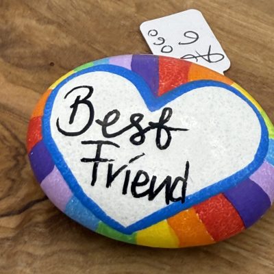 Enhance your decor with a unique hand-painted rock featuring a vibrant rainbow border, set against a rustic wooden surface. This beautifully crafted rock prominently displays a white heart in the center adorned with bold black letters that spell Best Friend. Perfect as a thoughtful gift or keepsake, this painted rock also comes with an attached small white tag for personalized writing or messages. Ideal for those searching for friendship gifts, DIY home accents, or personalized decorations.