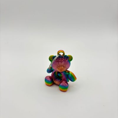 A vibrant tie-dye teddy bear keychain stands out against a plain white background. This colorful rainbow teddy bear features swirly eyes and a round nose, with its limbs showcasing bright hues. Attached to the top is a durable metal keyring, making it an eye-catching accessory for your keys or bag.