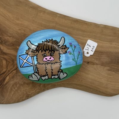 Discover this charming hand-painted rock showcasing a whimsical cartoon Highland cow with a delicate flower in its mouth. Set against a vivid blue background, this unique piece features the iconic Scottish flag alongside vibrant purple flowers. Perfectly displayed on a rustic wooden slab, this collectible art piece is priced at just £5. Ideal for those seeking Scottish-themed painted rocks or Highland cow gifts!.