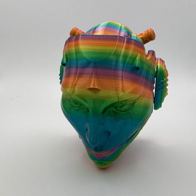 The 3D Printed Droid Mask is an eye-catching sculpture featuring a stylized human face with vivid rainbow stripes, embodying the essence of a futuristic droid. It showcases striking exaggerated features and unique cylindrical elements on the head, amplifying its artistic appeal.