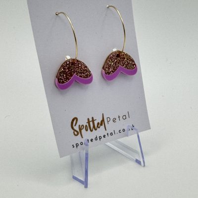 Heart-shaped glitter earrings with gold hooks and a pink border, showcased on a Spotted Petal card, elegantly displayed on a clear jewelry stand.