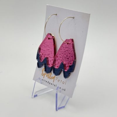 Enhance your style with our eye-catching pink and blue acrylic wavy earrings, elegantly hanging from a circular metal hoop. These unique earrings are beautifully showcased on a branded card stand featuring spottedpetal.co.uk at the bottom. The simple white background highlights their vibrant colors.