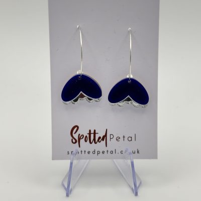 Discover the elegance of our dark blue and silver heart-shaped pendant earrings, beautifully presented on a Spotted Petal branded card. These stunning earrings stand gracefully on a clear display against a sleek gray background. Perfect for those seeking stylish heart pendant jewelry with a touch of sophistication.