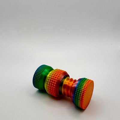 A vibrant, multicolored cylindrical object with textured surfaces on each end, similar to a popular fidget toy, is displayed against a stark white background. The colors seamlessly transition across the entire rainbow spectrum. This eye-catching fidget gadget offers both visual appeal and tactile engagement.