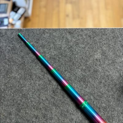 Discover the striking 3D Printed Telescopic Sword with vibrant gradient colors including purple, blue, green, and orange. This unique telescopic sword lies elegantly on a gray surface, beautifully offset by a wooden floor and shelving in the background. Perfect for collectors and enthusiasts looking for eye-catching 3D printed swords or gradient-colored weapons.