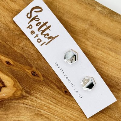Elegant hexagonal black and silver earrings from Spotted Petal showcase their unique design on a stylish card, elegantly placed on a rustic wooden surface.