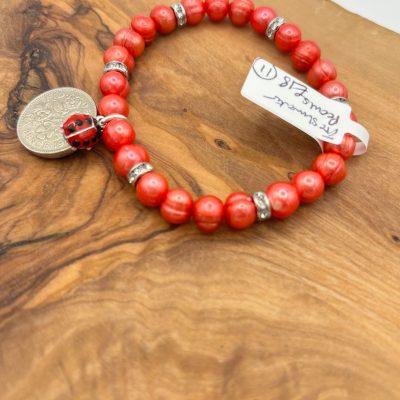 Enhance your jewelry collection with the Coral Peach Pearl Bracelet, beautifully adorned with elegant silver spacers, a cute ladybug charm, and a stylish round silver coin charm. This handmade beaded bracelet is showcased on a rustic wooden surface and comes with an attached white handwritten tag for a personalized touch. Perfect as a unique gift or chic accessory, this coral pearl bracelet adds sophistication and playful charm to any outfit.