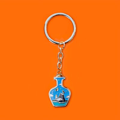 Discover the perfect addition to your keyring collection with this stunning blue bottle-shaped keychain. Featuring a durable silver ring and chain, this accessory showcases an intricately designed ship complete with masts and sails set against a vibrant orange backdrop. Ideal for enhancing your Puffin in a Bottle enamel pin collection, this unique keychain is perfect for nautical enthusiasts looking to make a statement.